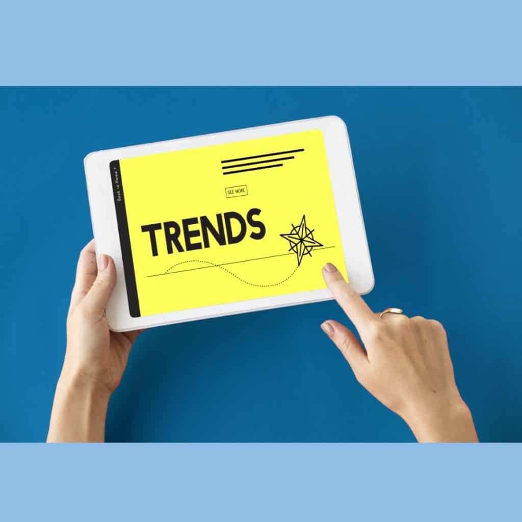 Hands holding a tablet, "trends" appears on the screen. Outsourcing market trends article